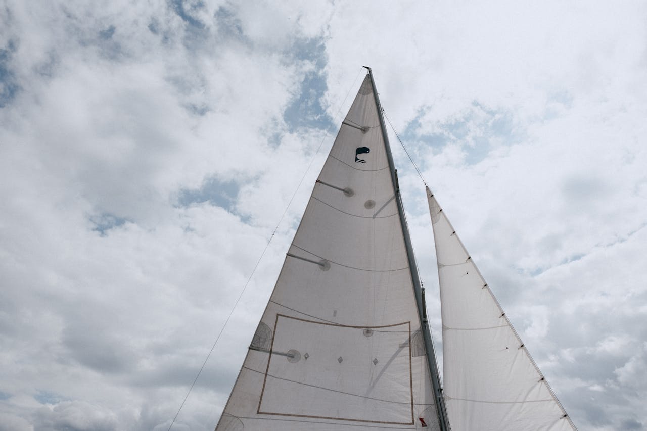 Capture the essence of sailing with a view of a yacht's sails soaring against the cloudy sky.