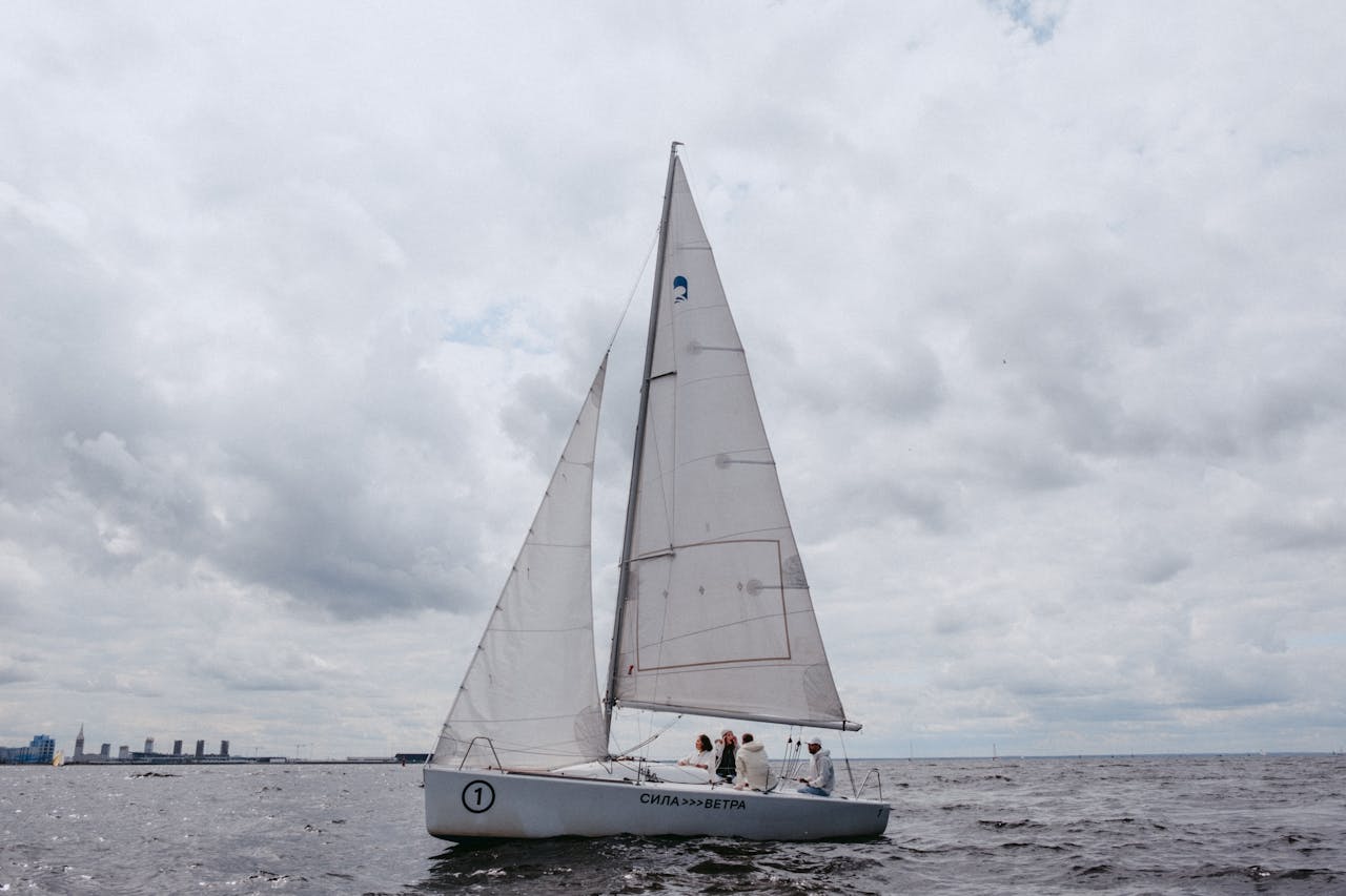 A yacht sailing on the ocean with a team onboard under a cloudy sky.