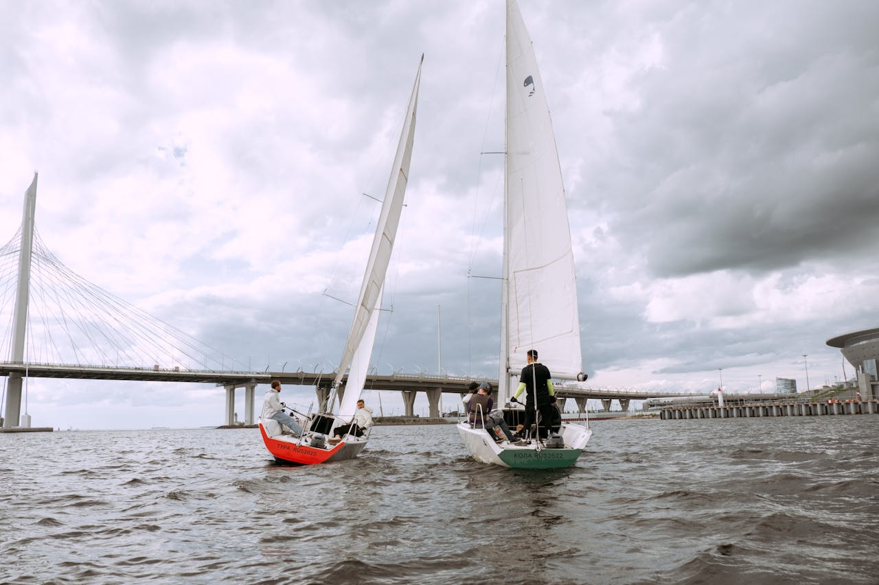 Two sailboats race under a bridge on a cloudy day, capturing the essence of nautical adventure.