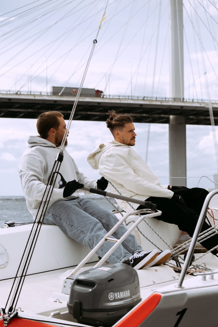 Two men sailing a yacht under a bridge on a clear day, enjoying the ocean view.